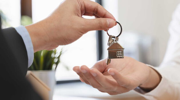 Schlüsselübergabe für neue Immobilie Übergabe eines Schlüsselbundes mit kleinem Hausanhänger an neuen Immobilienbesitzer